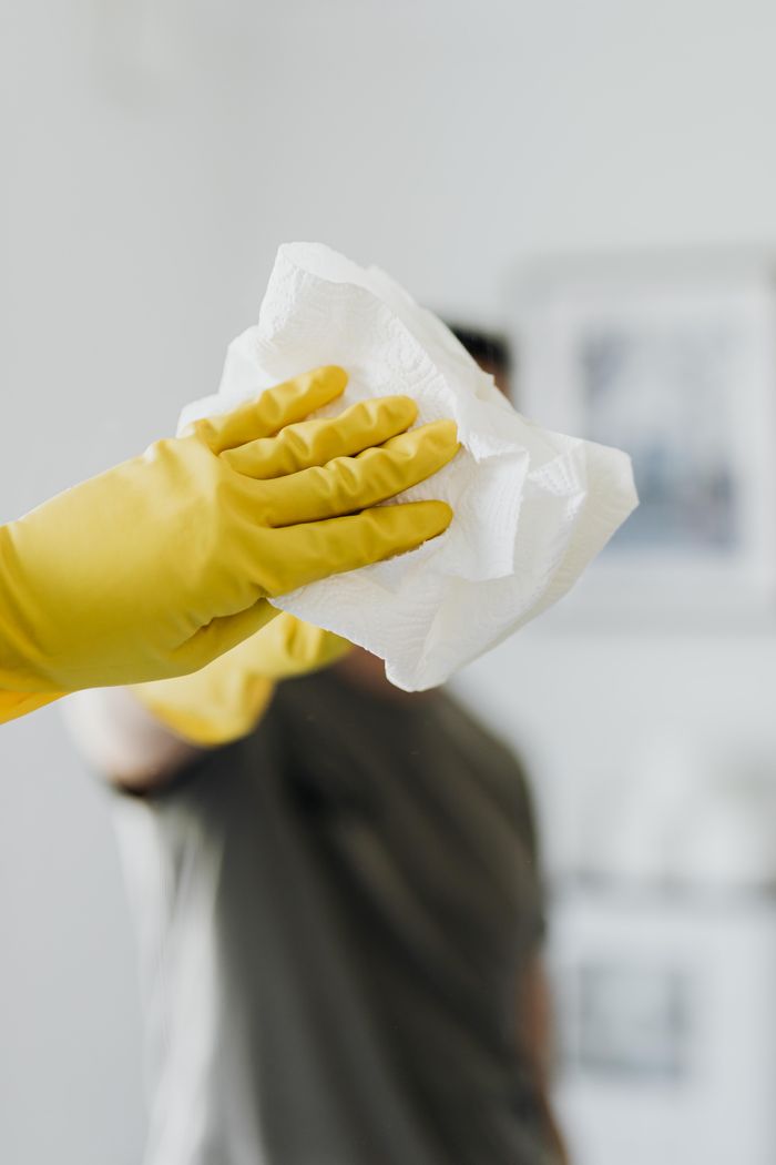 gallery-01 Anonymous male wearing yellow latex gloves and dark t shirt wiping mirror in bathroom with paper napkin